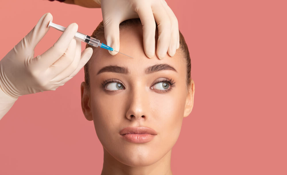 Woman receiving a forehead injection, likely BOTOX® or a similar cosmetic injectable, to reduce fine lines and wrinkles.